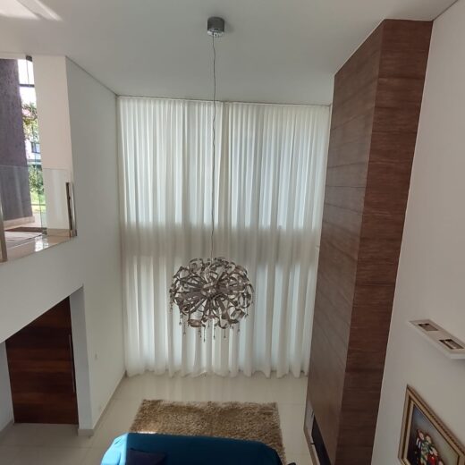 Cortina translúcida em sala com pé-direito duplo: a automação permite controlar a entrada de luz com um comando.